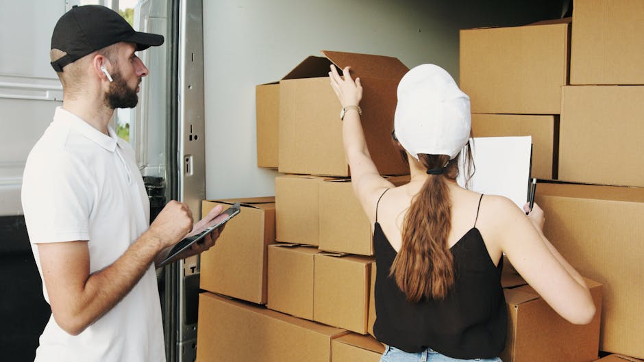 Two individuals engaged in home relocation activities at a residential property, with a focus on furniture transport and packing for a move. On the left, a man wearing a black cap, white t-shirt, and